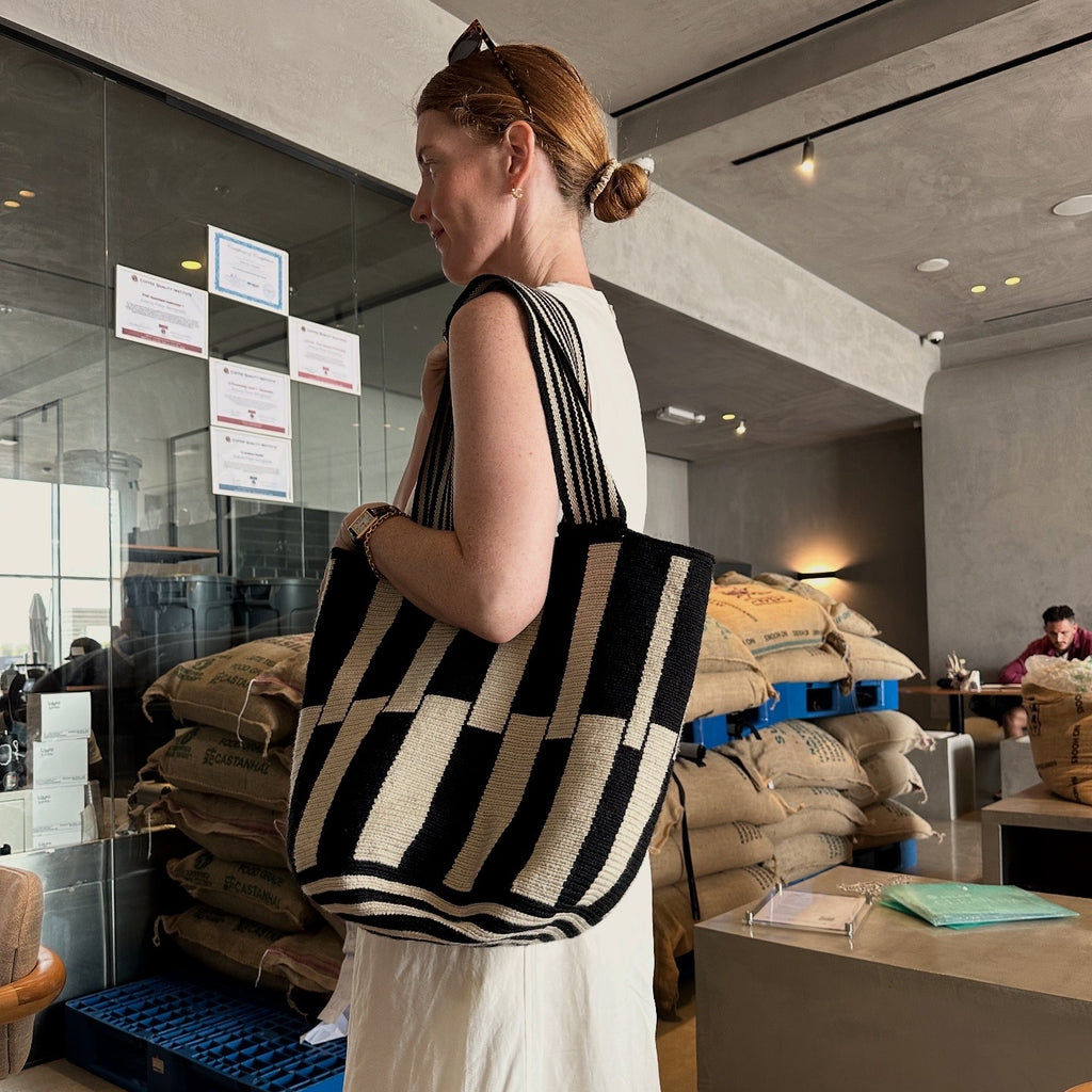 PALANACHI Stripped tote bag in beige and black by iiwa kashi, handcrafted by Wayuu artisans in La Guajira, Venezuela, made with pure cotton and 24K gold-plated silver logo.