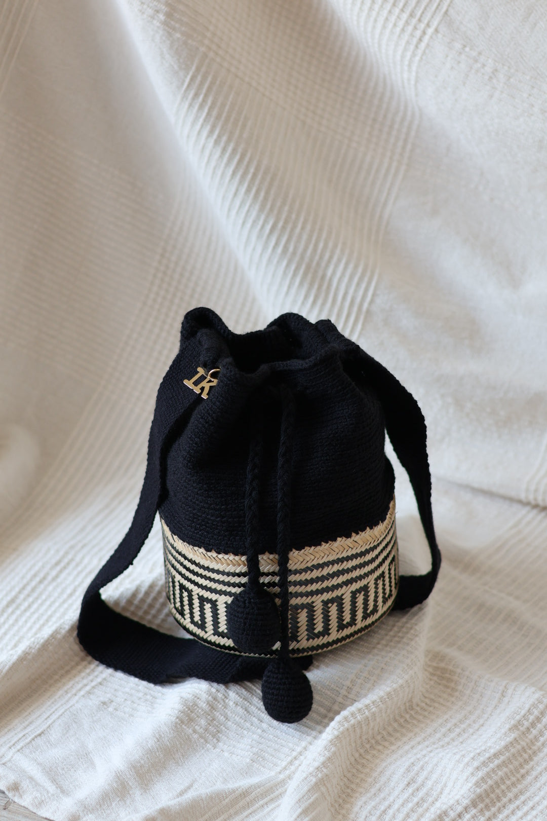 La Canasta Bag in black by iiwa kashi, handcrafted by Wayuu artisans in Venezuela with cotton and caña brava, featuring 24K gold-plated logo.