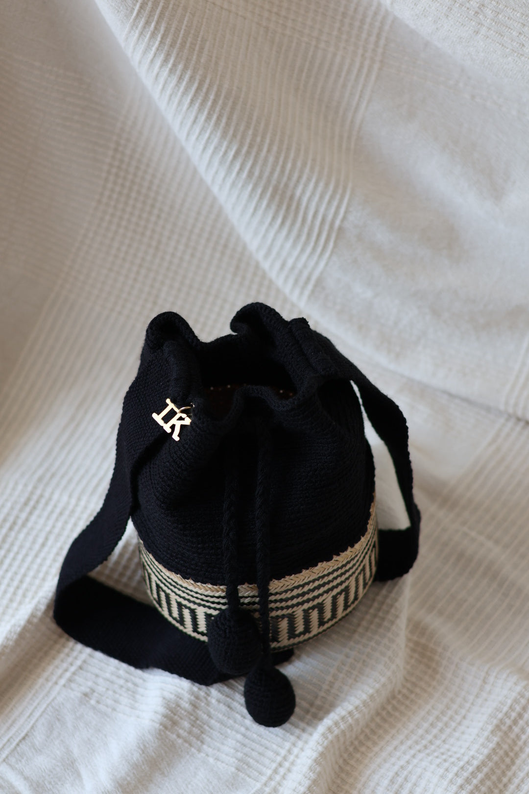 La Canasta Bag in black by iiwa kashi, handcrafted by Wayuu artisans in Venezuela with cotton and caña brava, featuring 24K gold-plated logo.
