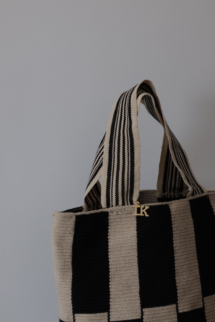 PALANACHI Stripped tote bag in beige and black by iiwa kashi, handcrafted by Wayuu artisans in La Guajira, Venezuela, made with pure cotton and 24K gold-plated silver logo.